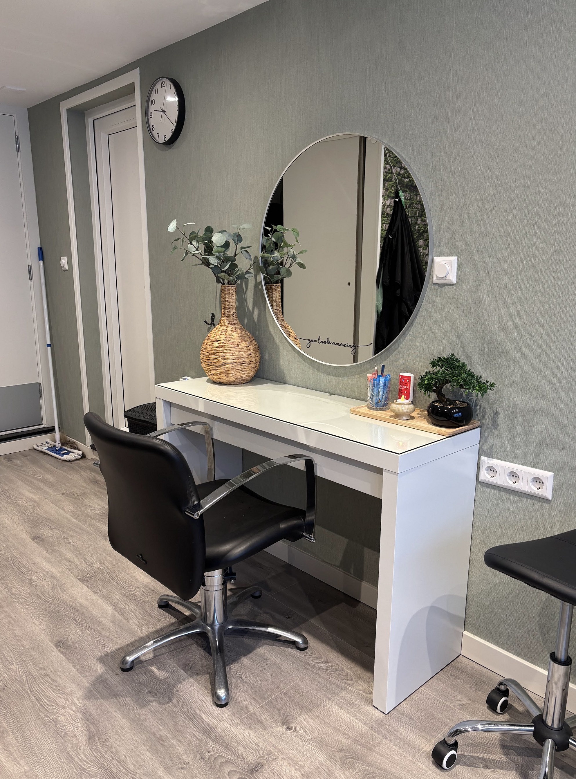 De werkplek van Hairsalon 23: ronde spiegel, witte kaptafel en zwarte kappersstoel